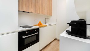 Moderni keittiö, jossa on valkoiset kaapit, musta uuni, kahvinkeitin ja leikkuulauta, jonka päällä on appelsiineja.