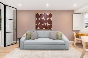 A modern living room with a grey sofa, two patterned throw pillows, a beige rug, and a large abstract painting on the wall. - Live Lisbon from the Famous Green Street (Lisbon)