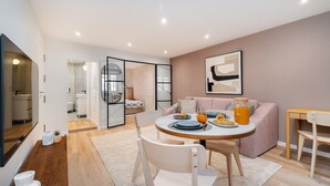 A modern kitchen with a dining area, featuring a round table with chairs, a sofa, and a breakfast setup with croissants and orange juice. - Live Lisbon from the Famous Green Street (Lisbon)