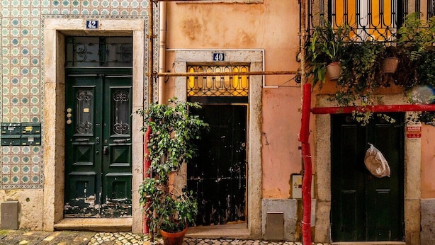 A building with two doors, one marked with the number 42 and the other with 40. There is a potted plant in front of the doors, and a red pipe runs along the wall. - Live Lisbon from the Famous Green Street (Lisbon)