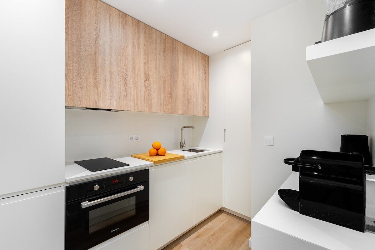 A modern kitchen with white cabinetry, a black oven, a wooden cutting board with oranges, and a coffee machine.