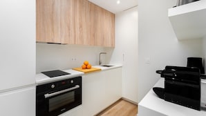 A modern kitchen with white cabinetry, a black oven, a wooden cutting board with oranges, and a coffee machine. - Live Lisbon from the Famous Green Street (Lisbon)