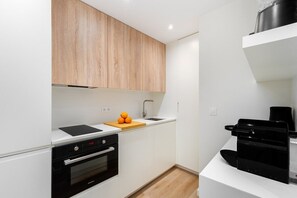 Eine moderne Küche mit weißen Schränken, einem schwarzen Backofen, einem Holztisch mit Orangen und einer Kaffeemaschine.