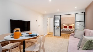A modern living room with a flat-screen TV, a dining area with a table and chairs, and a sofa with cushions. - Live Lisbon from the Famous Green Street (Lisbon)