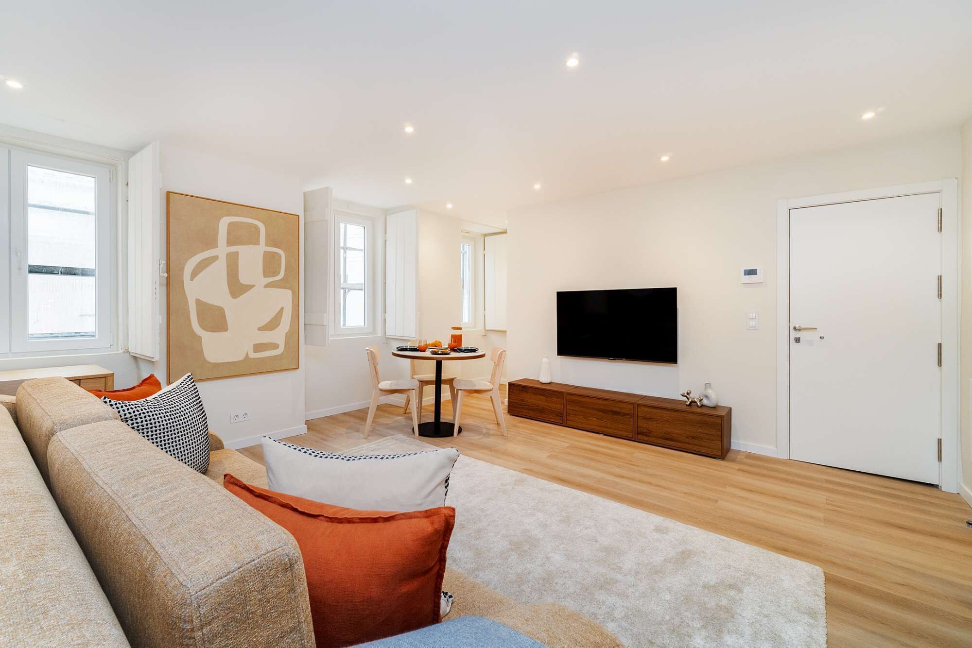 A modern living room with a sofa, a dining area with chairs, a TV, and a white door.