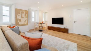 Uma sala de estar moderna com um sofá, uma área de refeições com cadeiras, uma televisão e uma porta branca.