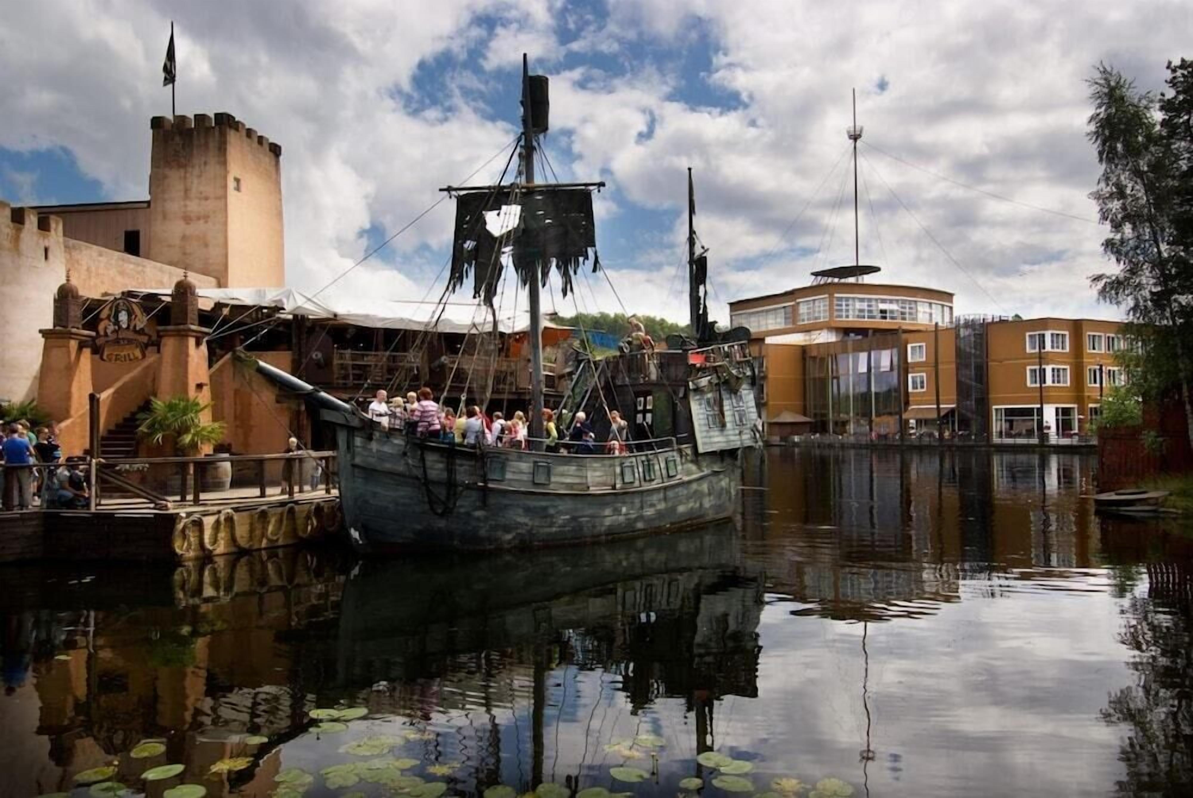 Un barco histórico amarrado en la costa, rodeado de edificios y un cielo despejado.