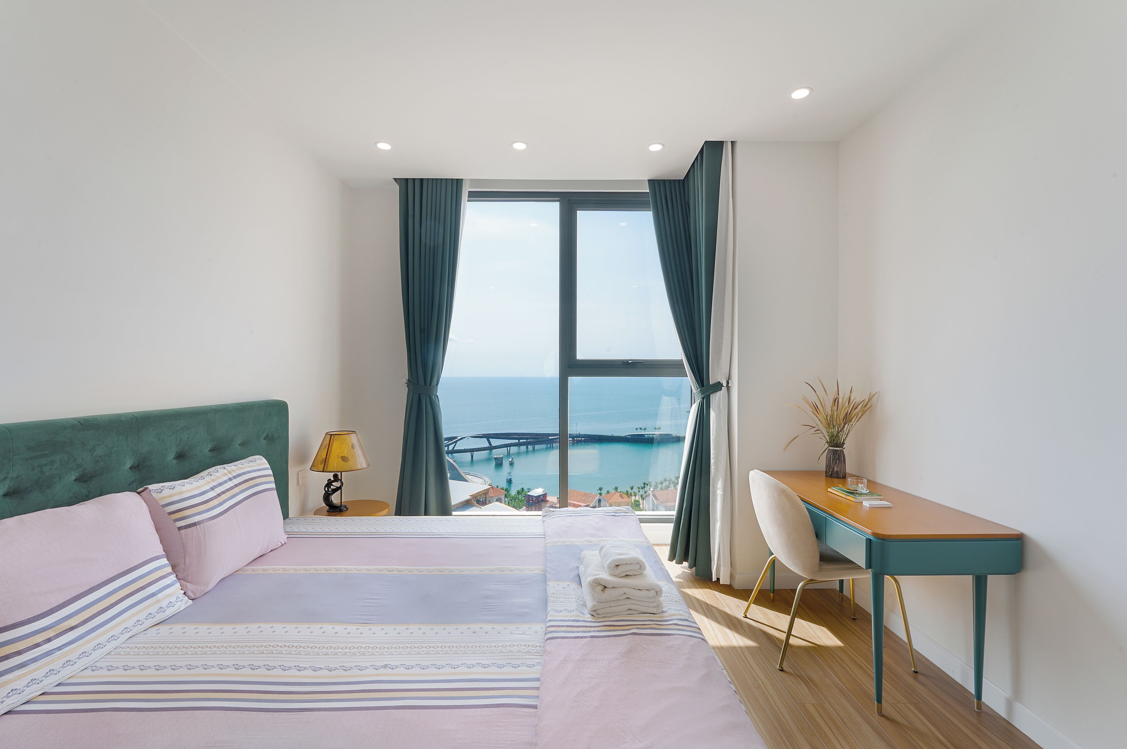 A bedroom with a bed, a desk, a chair, and a view of the sea.