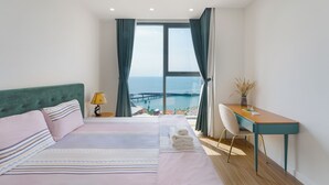 Um quarto com cama, escrivaninha, cadeira e vista para o mar.
