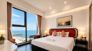 Un cuarto de hotel con un ventanal grande, una cama con sábanas blancas, dos lámparas de noche y un cuadro en la pared.