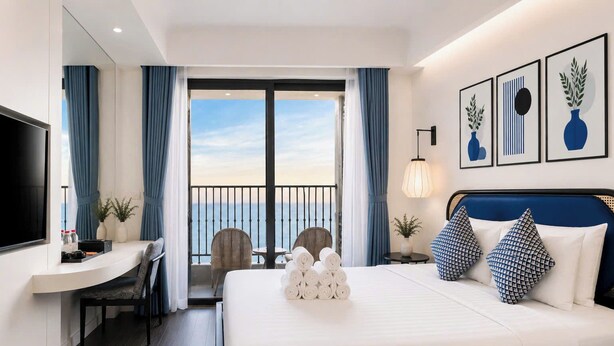 Habitación de hotel con cama, escritorio, silla, televisor y balcón con vistas.
