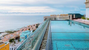 Piscina infinita en la azotea con vistas al océano y edificios costeros.