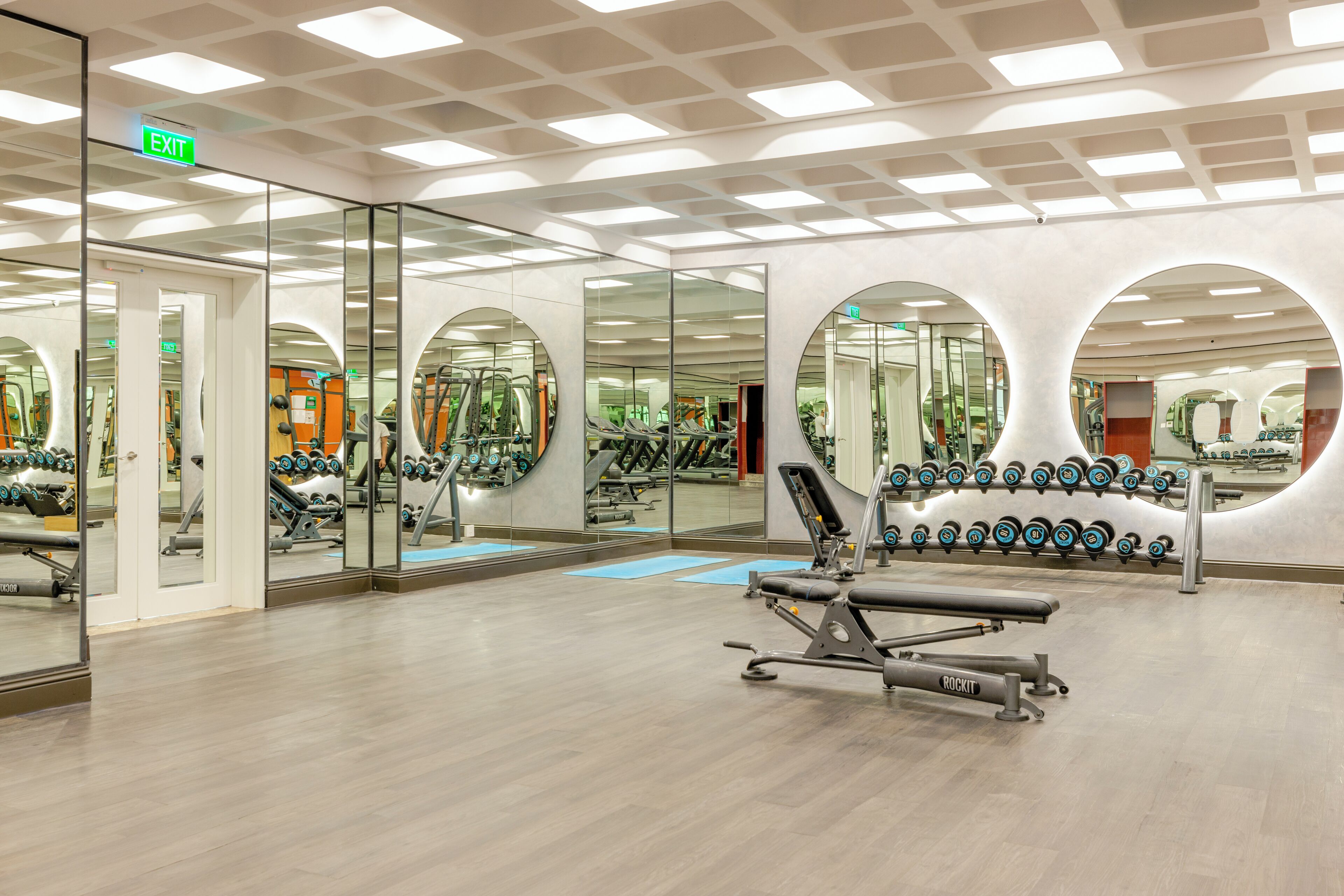 Ett gym med spegelbeklädda väggar, träningsutrustning och ett ställ för vikter.