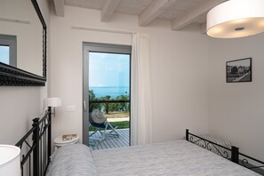 A bedroom with a bed, a chair, a small table, a mirror, a picture on the wall, and a view of the sea through a door. - Appartamenti Arca and Ca Mure (Bardolino)