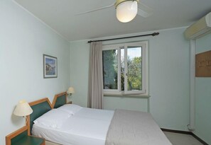 A bedroom with a bed, a window with curtains, a ceiling fan, and a wall-mounted lamp. - Appartamenti Arca and Ca Mure (Bardolino)
