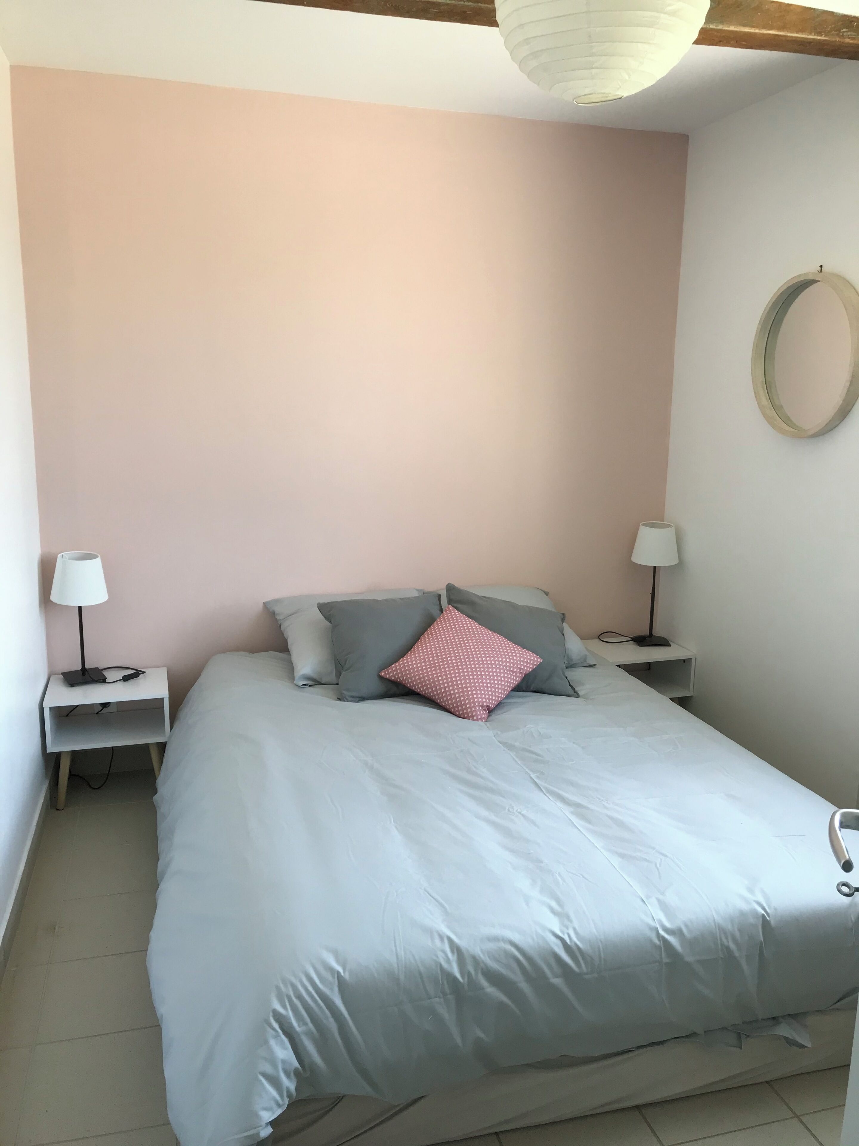 Een slaapkamer met een groot bed, twee nachtkastjes met lampen, een ronde spiegel aan de muur en een plafondlamp.