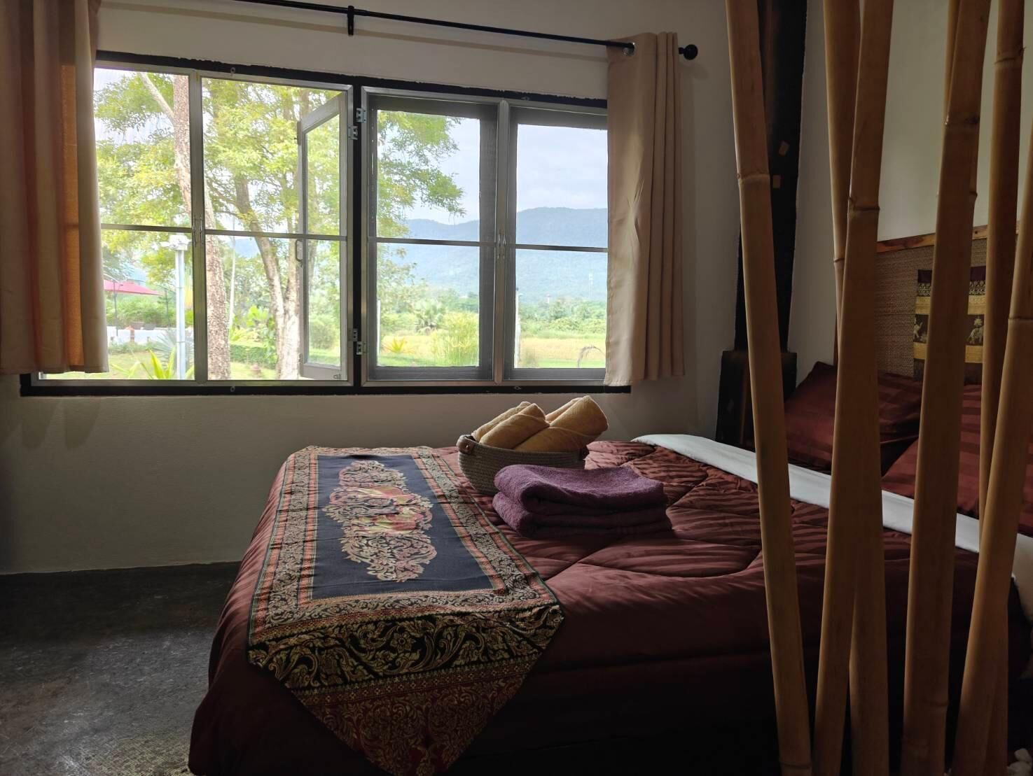 Ein Zimmer mit einem Bett, einem Fenster mit Blick auf Grünflächen und Hügel sowie einem Vorhang.
