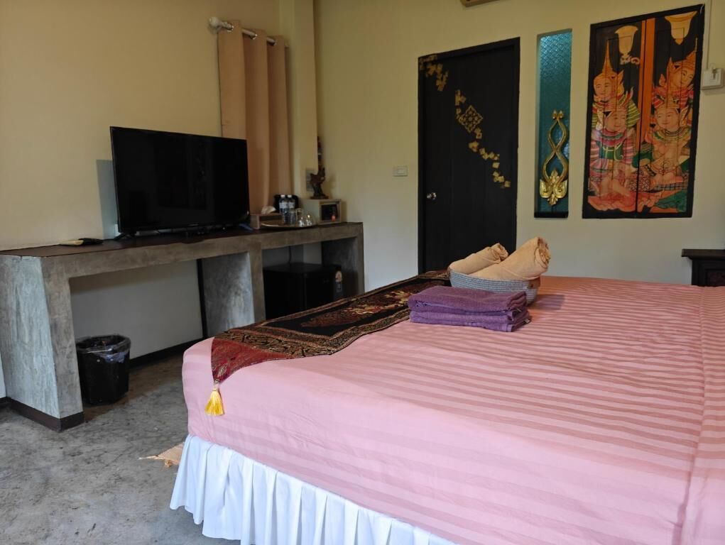 A room with a bed, a desk with a television, a trash bin, and two doors.