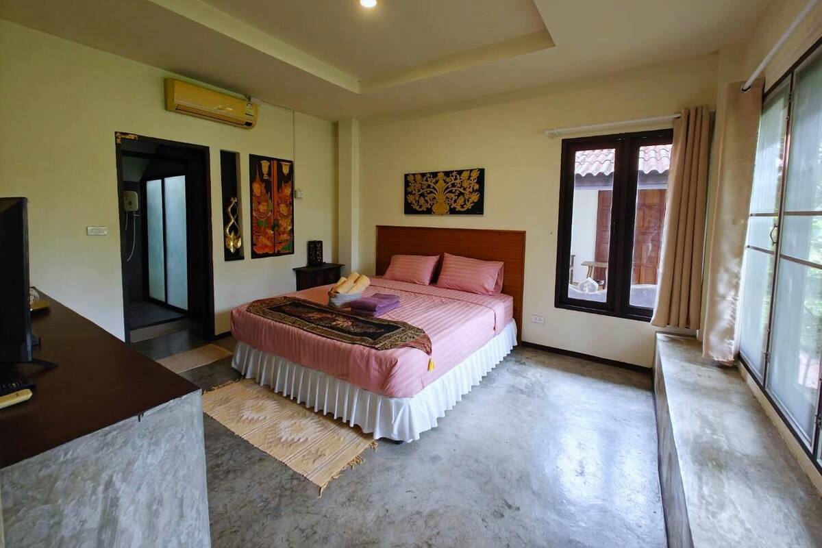 A bedroom with a bed, a desk, a window, and artwork on the walls.