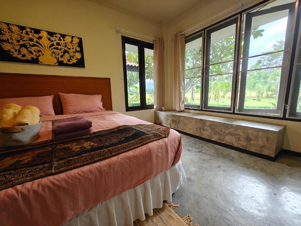 Un dormitorio con una cama grande, un asiento junto a la ventana y vista a zonas verdes.