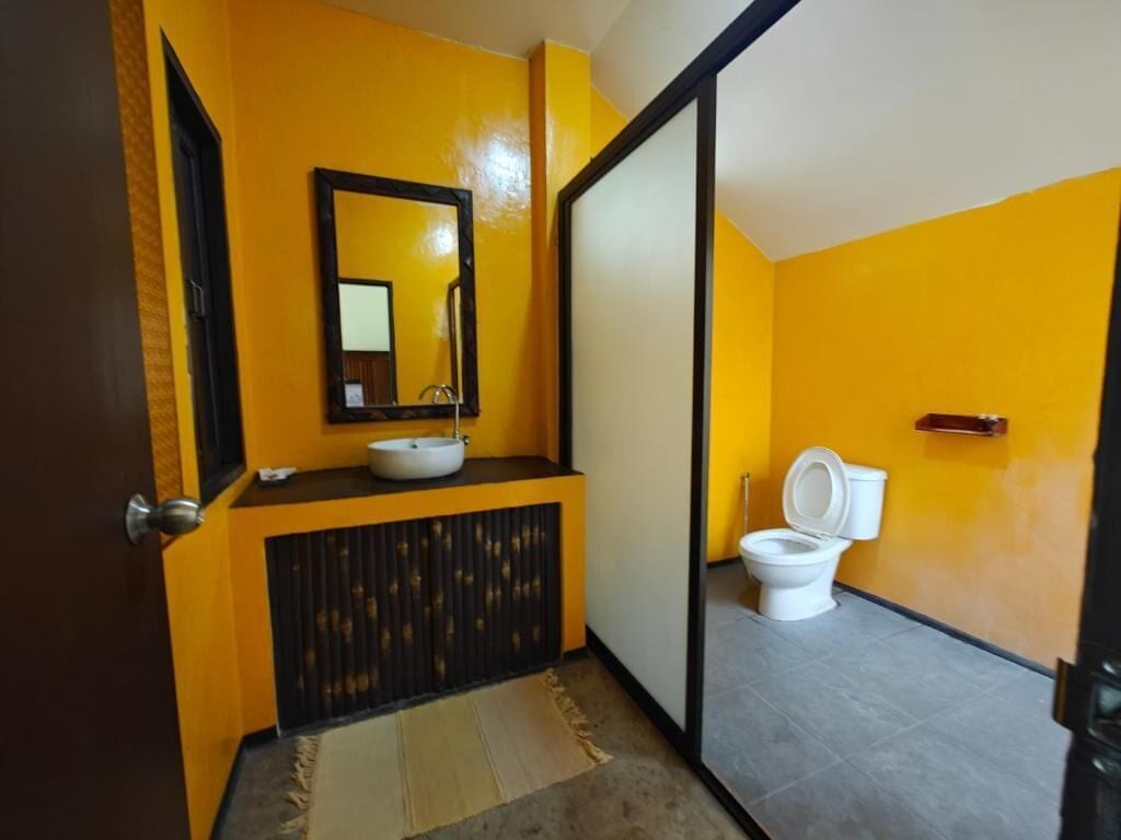 A bathroom with a yellow wall, a black-framed mirror, a white sink, and a toilet.