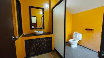 A bathroom with a yellow wall, a black-framed mirror, a white sink, and a toilet.