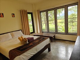 Un dormitorio con cama, una banca y ventanas amplias que dan a zonas verdes.