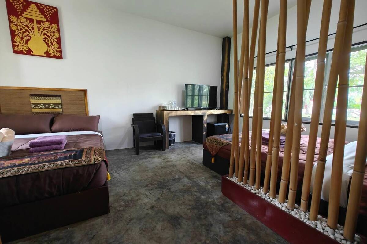 A hotel room with a bed, a desk with a computer, a TV, and a large window with bamboo blinds.