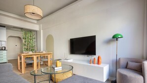 Un soggiorno moderno con zona pranzo, televisore a schermo piatto, lampada da terra verde e divano grigio.