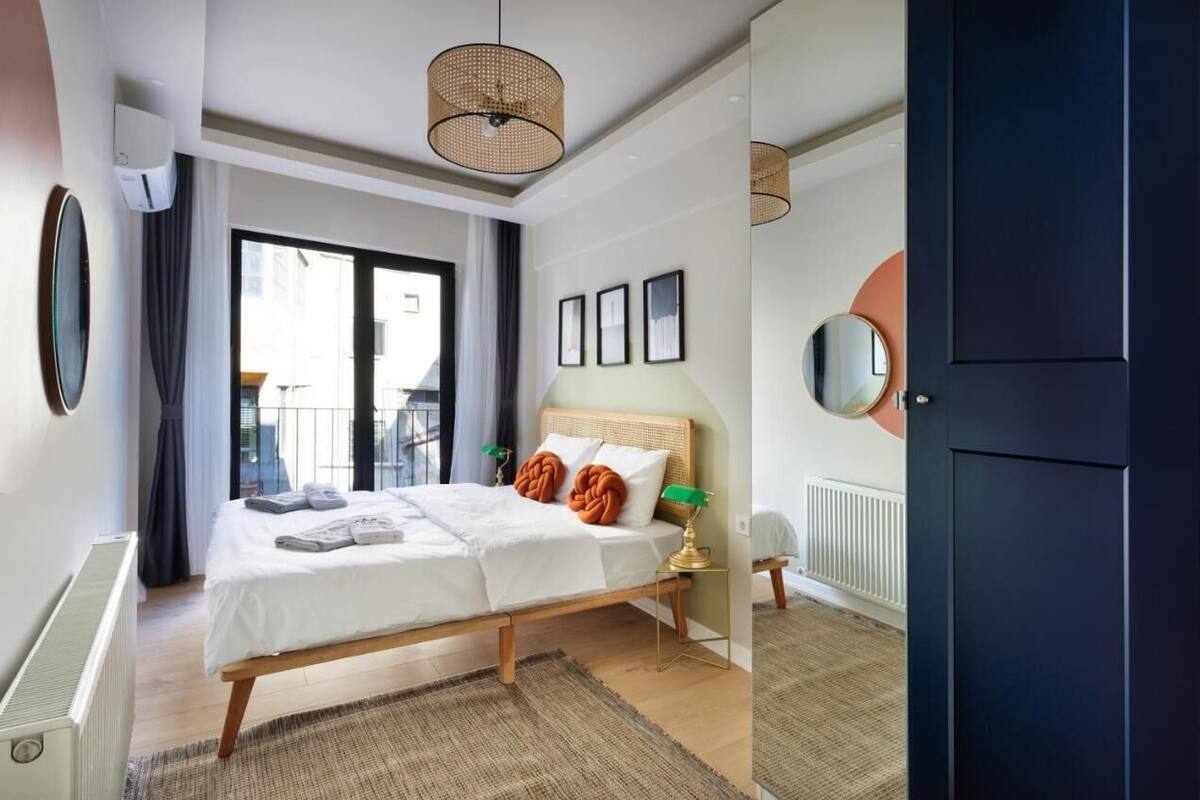 A modern hotel room with a large bed, bedside lamps, a mirror, and a view of the city.