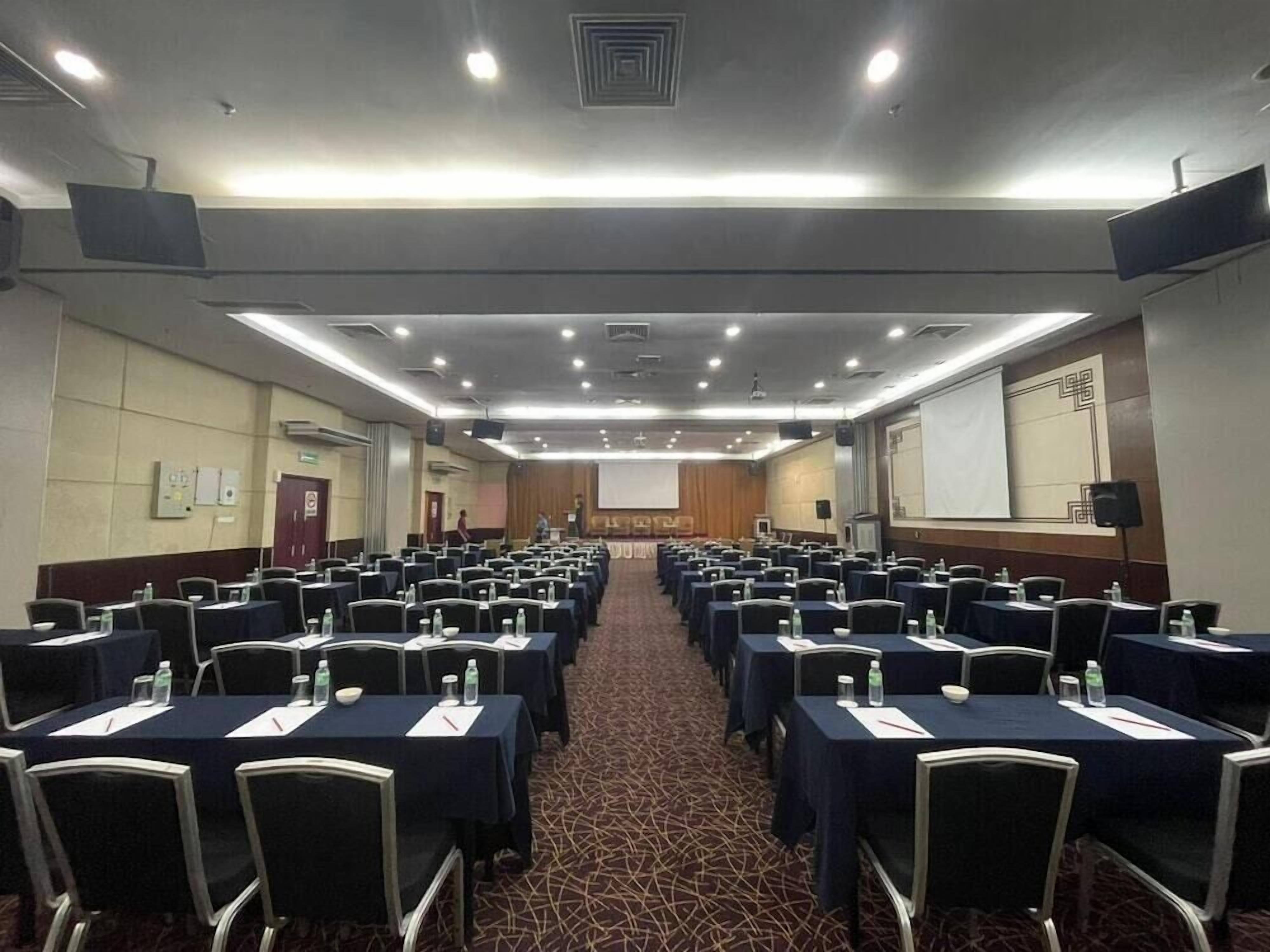 Una sala conferenze con file di tavoli e sedie, dotata di proiettori e schermi.
