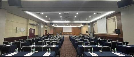 Una sala conferenze con file di tavoli e sedie, dotata di proiettori e schermi.