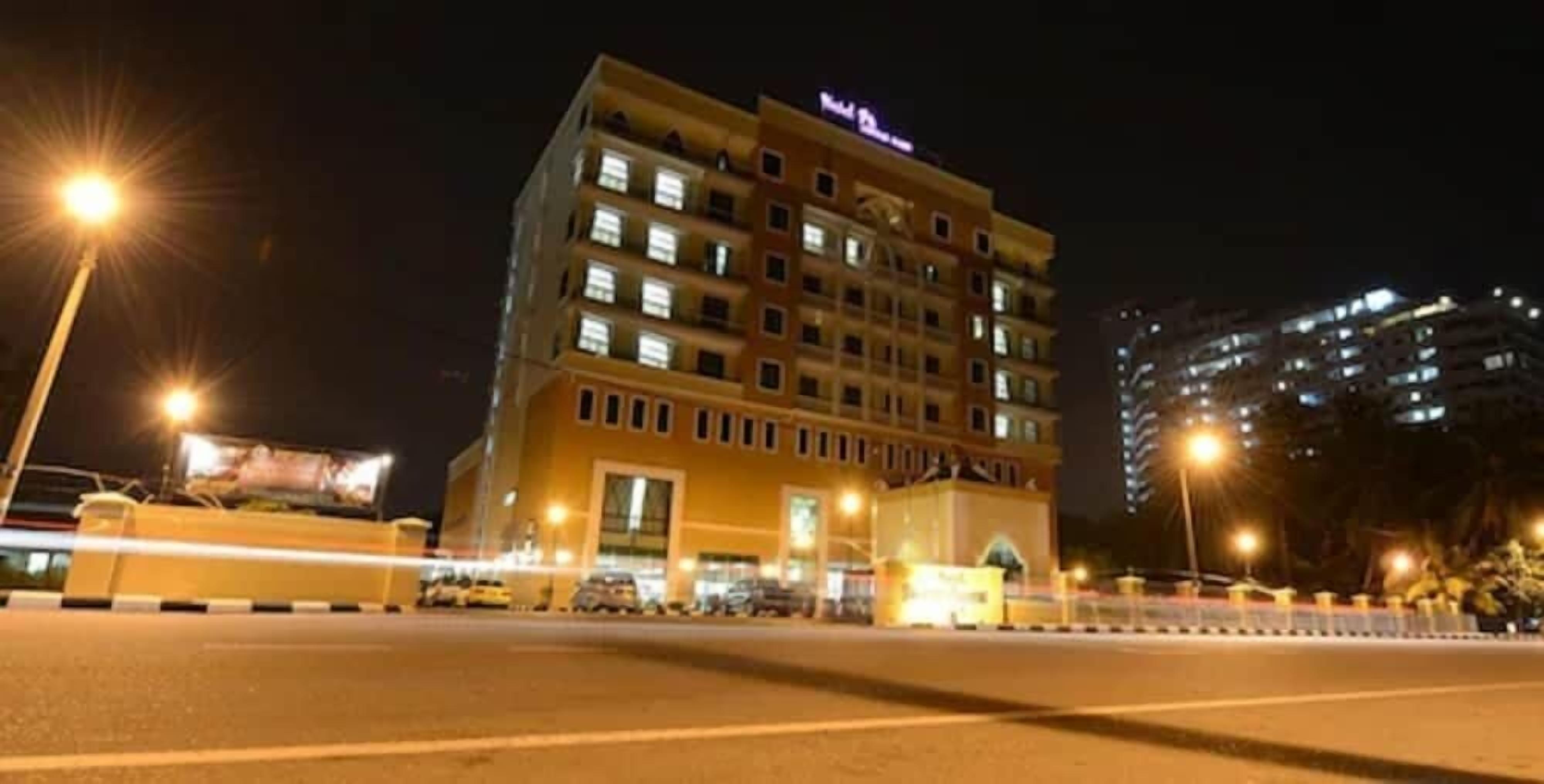 A multi-story hotel with illuminated windows, a prominent entrance, and a parking area in front.