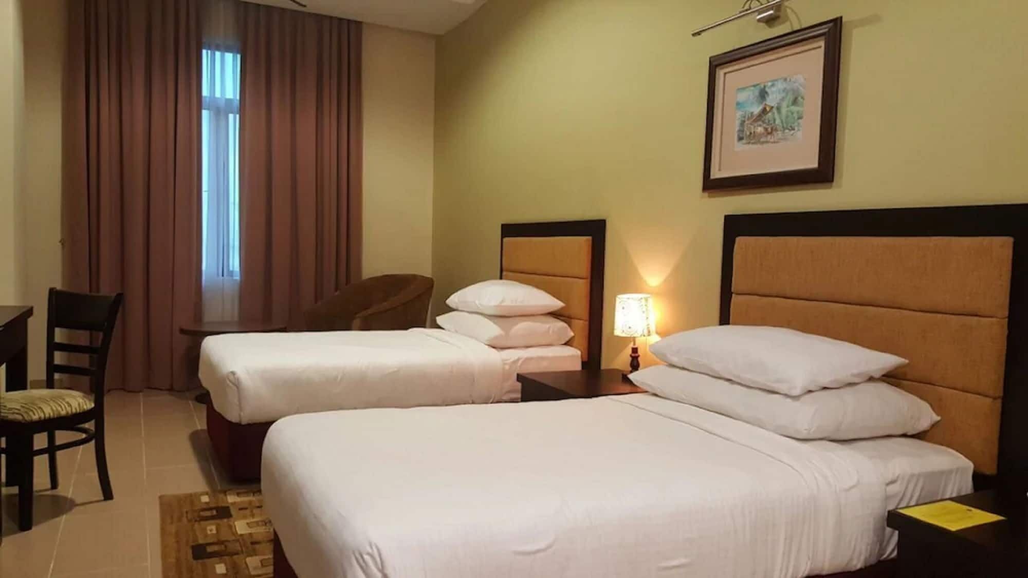 A hotel room with two beds, a desk, a chair, and a window with curtains.