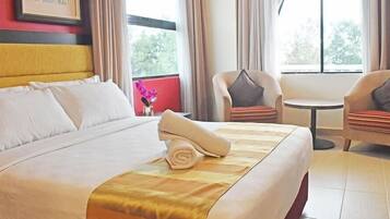 A hotel room with a large bed, two armchairs, a small table, and a window with curtains.