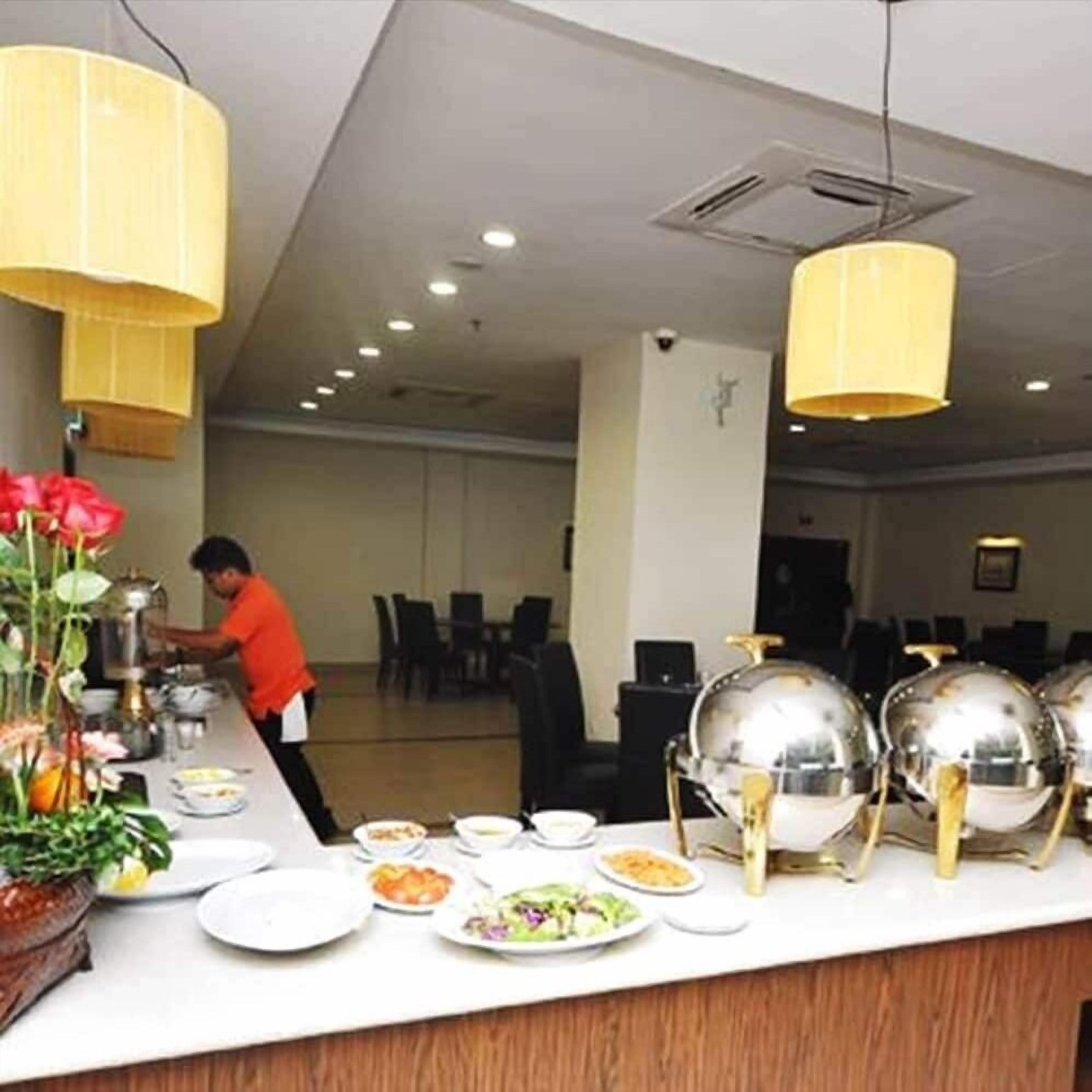 A buffet setup with various dishes, a chef preparing food, and a modern interior with hanging lamps.