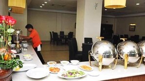 Ein reichhaltiges Buffet mit verschiedenen Speisen, ein Koch bereitet etwas zu und ein modernes Ambiente mit Hängeleuchten.