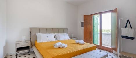 A bedroom with a bed, a bench, a nightstand, a window, and a door.