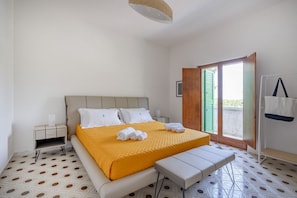A bedroom with a bed, a bench, a nightstand, a window, and a door.
