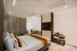 A hotel room with a bed, a desk, a chair, a television, and a ceiling fan. - Marugarh (Jodhpur)