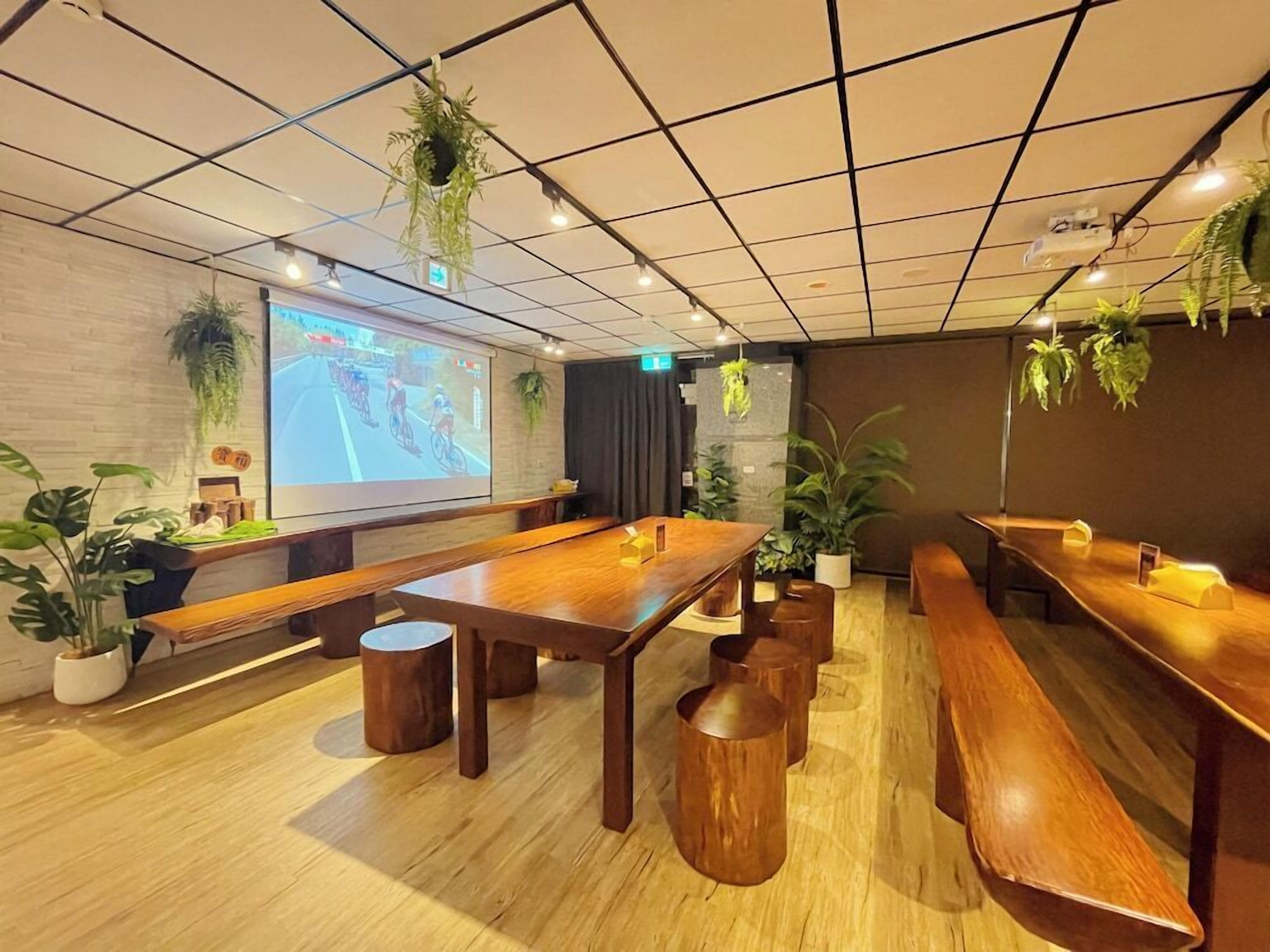 Un salón de conferencias con una larga mesa, bancos y plantas en macetas.