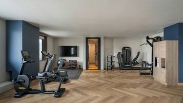 Uma academia moderna em casa com equipamentos de exercício, uma televisão e piso de madeira.