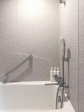 A modern bathroom with a bathtub, a showerhead, and toiletries on a shelf. - Hotel Crown Palais Kobe (Kobe)