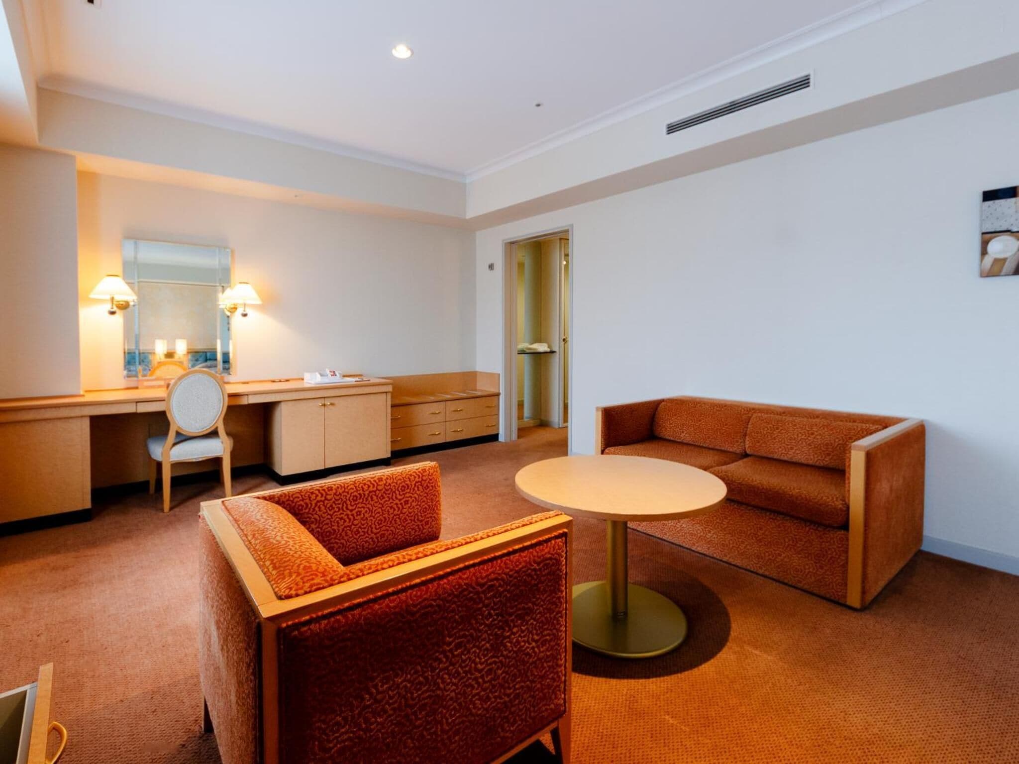 Quarto de hotel com uma escrivaninha, uma mesa redonda, um sofá e uma cadeira.
