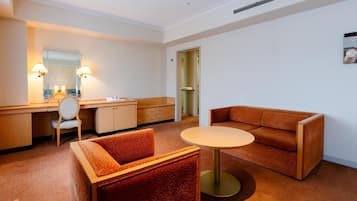 Quarto de hotel com uma escrivaninha, uma mesa redonda, um sofá e uma cadeira.
