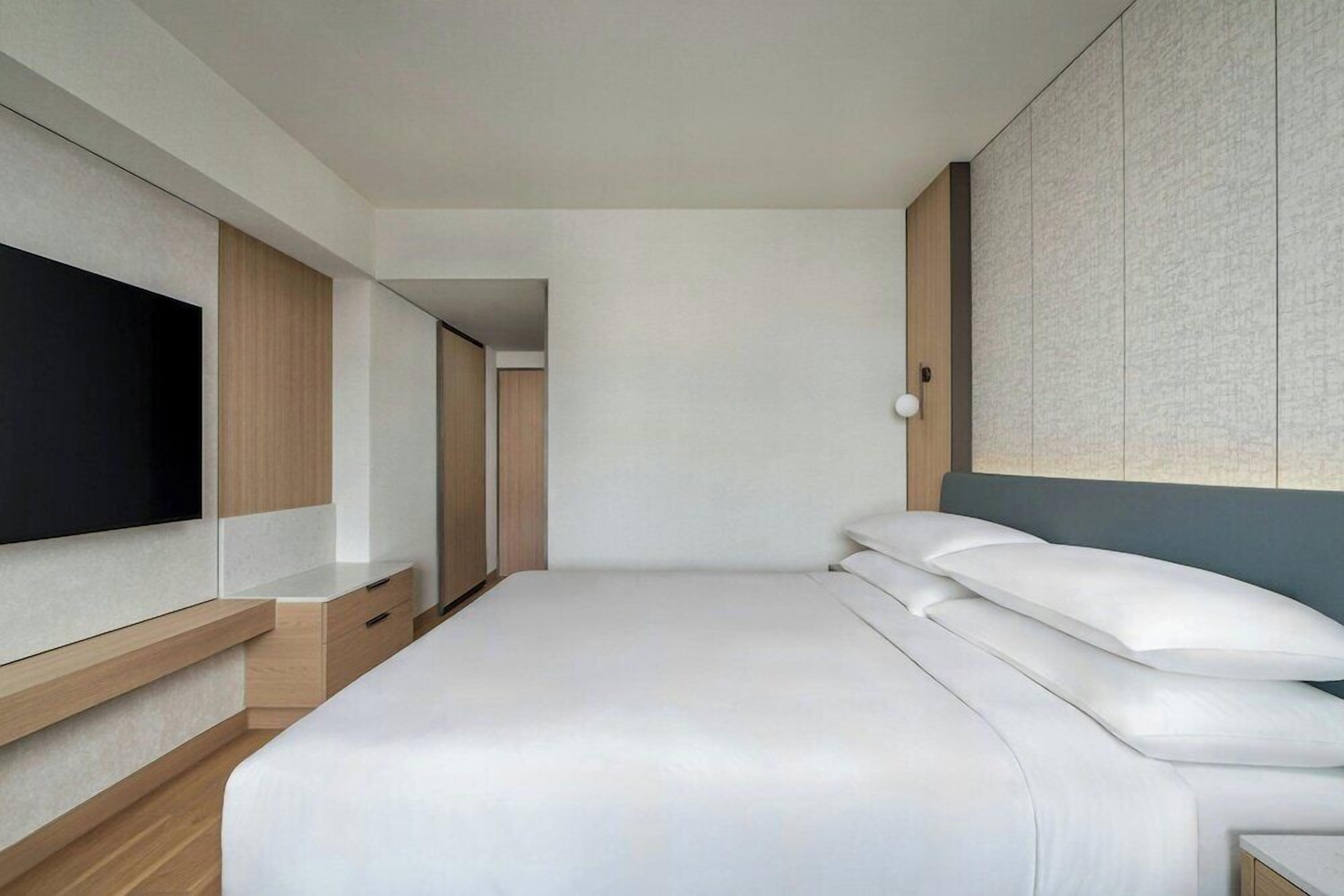 Quarto de hotel moderno com uma cama grande, televisão integrada e um guarda-roupa.