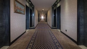 A long, narrow hotel corridor with patterned carpet, dark walls, and doors on both sides. - Vienna Hotel (Dongguan)