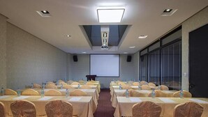 A conference room with rows of tables, each with a water bottle and a name card. There is a projector screen at the front and a speaker on the left. - Vienna Hotel (Dongguan)