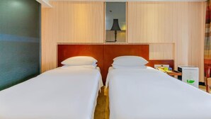 A hotel room with two single beds, a wooden headboard, a small desk with a lamp, and a minibar. - Vienna Hotel (Dongguan)