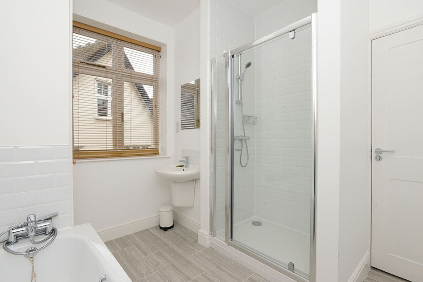 A modern bathroom with a glass-enclosed shower, a sink, and a window with blinds.